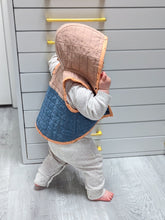 load image into gallery viewer, Baby wearing a quilted vest with a hood in a room with white walls and white floor.